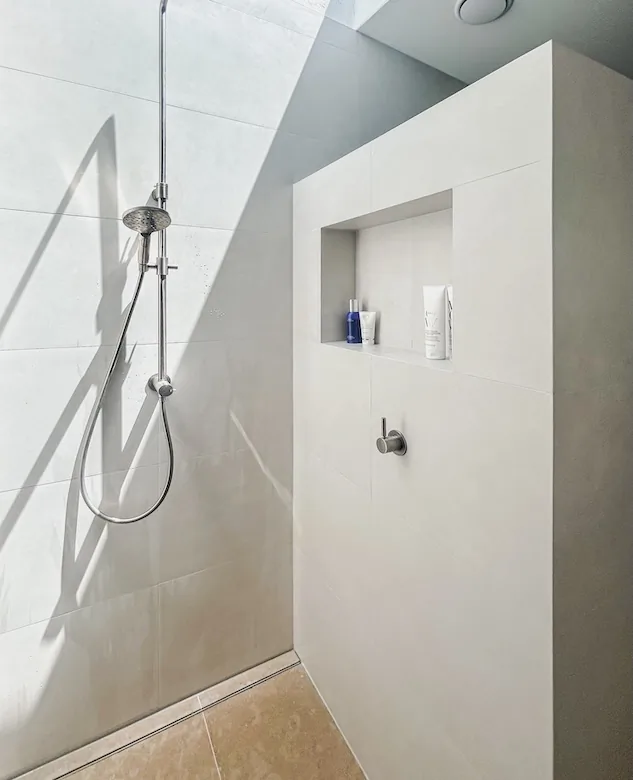 Large-format tiled shower divider wall with a recessed niche and mitred outer edge