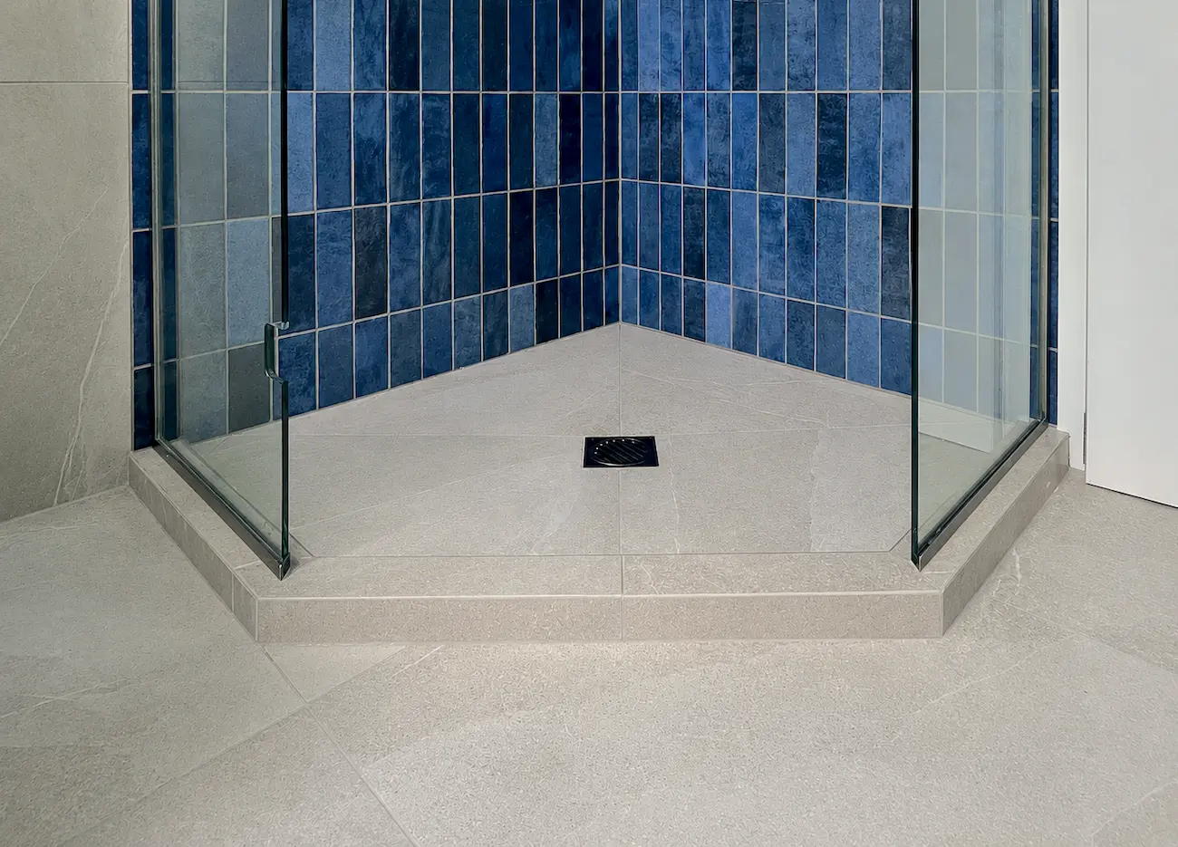 Finished shower base with mitred porcelain curb and blue finger-tile walls